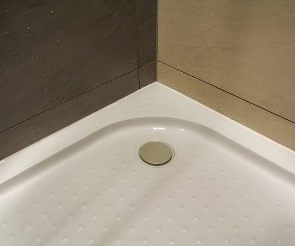 Close-up detail of new modern clean empty white shower cabin with drops of water on nice light beige ceramic tiles on floor and walls. Comfort and hygiene concept.