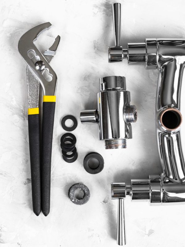 plumbing background - top view of wrench, disassembled shower faucet valve, diverter, spout, gaskets on concrete board with copyspace