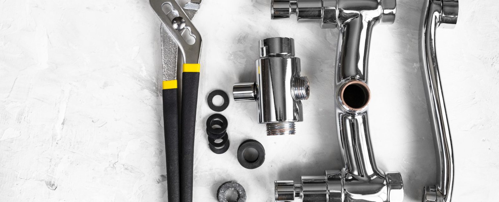 plumbing background - top view of wrench, disassembled shower faucet valve, diverter, spout, gaskets on concrete board with copyspace